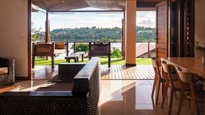 A modern interior with a wooden dining table, chairs, and a bench. A large window offers a view of a green landscape and a body of water. - Fatumaru Lodge Port Vila (Port Vila)