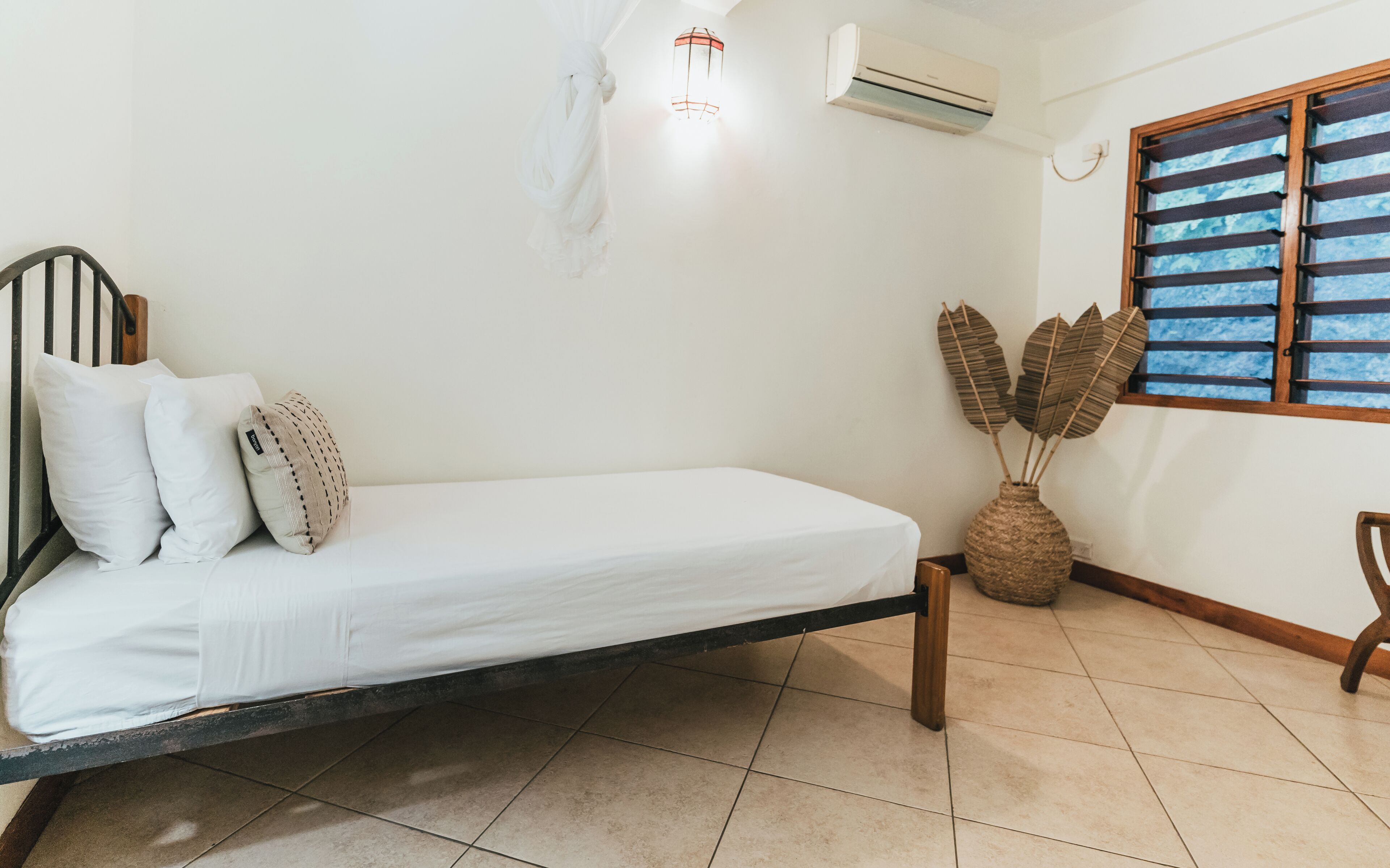 A single bed with a wooden frame, white bedding, and a woven plant pot on the floor.