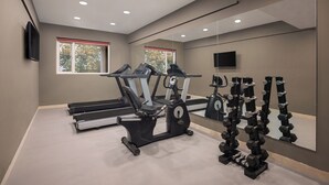 Un gimnasio con cintas de correr, una elíptica y un estante con mancuernas.