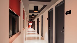 Un pasillo moderno de hotel con varias puertas, letreros numerados y una pared de acento roja.