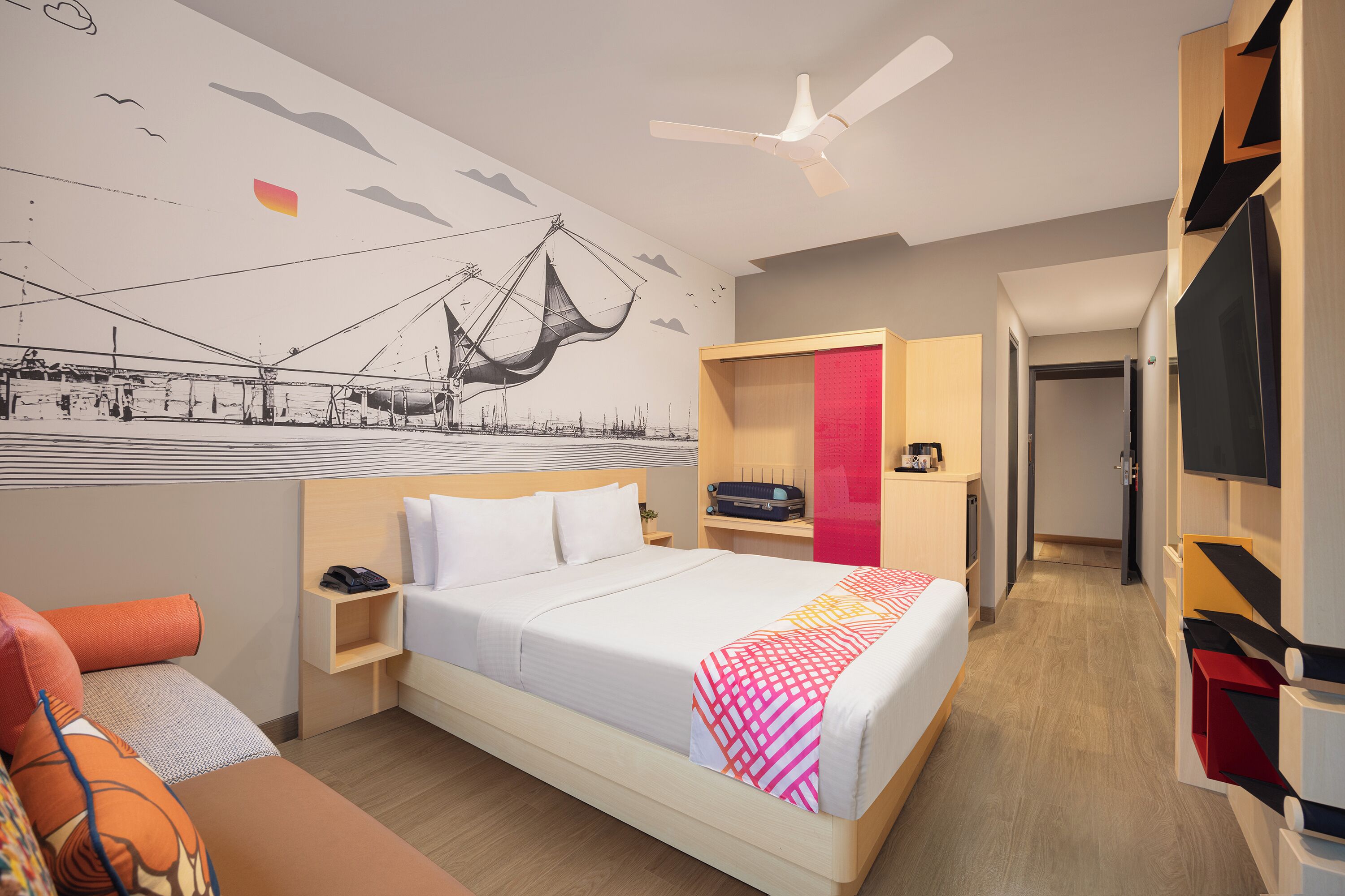 A modern hotel room with a large bed, a desk, a TV, and a mural on the wall.
