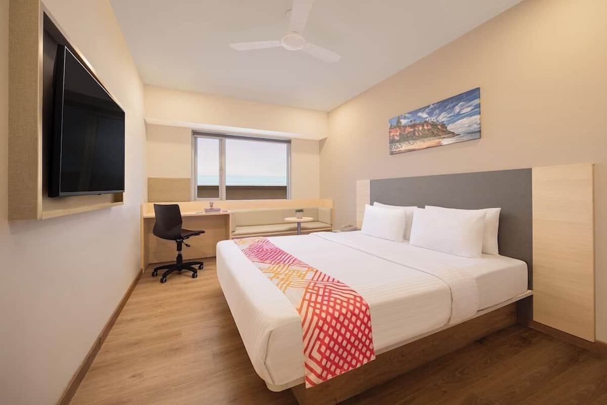 A hotel room with a bed, a desk, a chair, a TV, a window, and a ceiling fan.