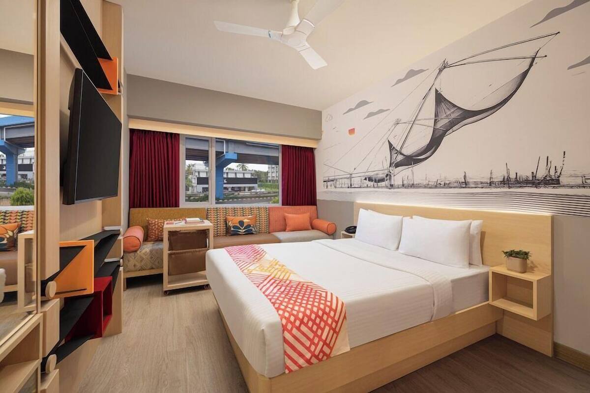 A hotel room with a bed, a desk, a TV, a window with curtains, and a mural on the wall.