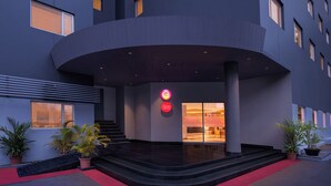 En moderne hotelindgang med en buet facade, rød løber og et tydeligt 'G' logo.