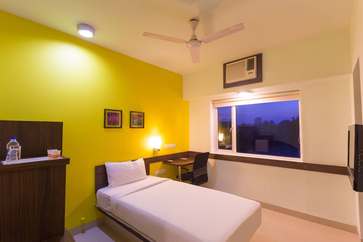 A hotel room with a bed, desk, chair, and a window with a view.