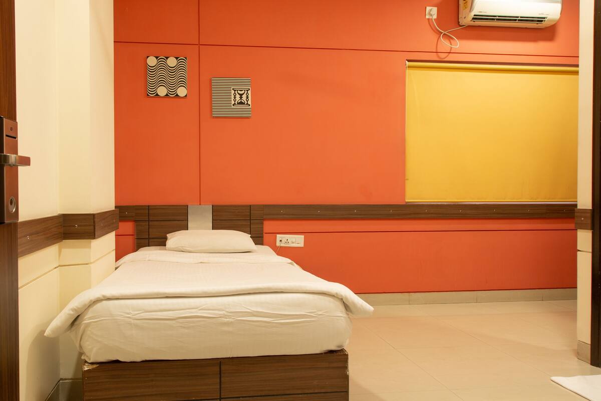 A hotel room with a bed, a wooden door, an air conditioning unit, and a yellow wall.