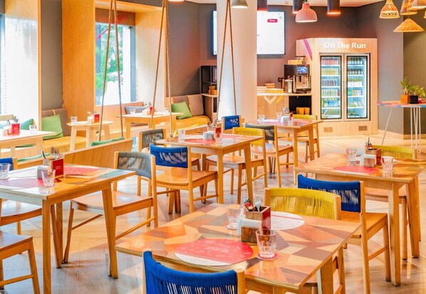 Un comedor moderno con mesas y sillas de madera, una zona de estar con cojines y un refrigerador que dice 'On The Run'.