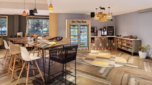 A modern cafe with a wooden table and chairs, a refrigerator labeled "On The Run," and a variety of snacks and drinks. - Ginger Durgapur (Durgapur)
