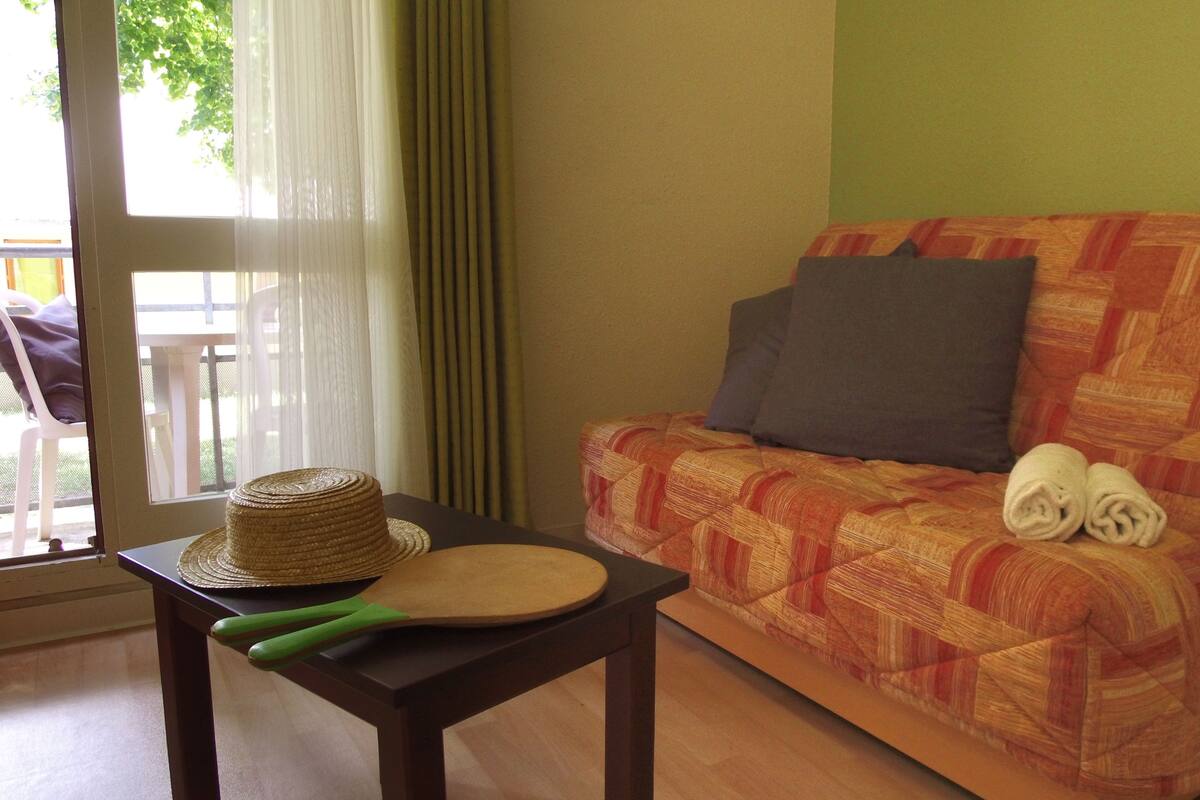 Een kamer met een bank, een tafel met een hoed en een peddel, en een raam met gordijnen.