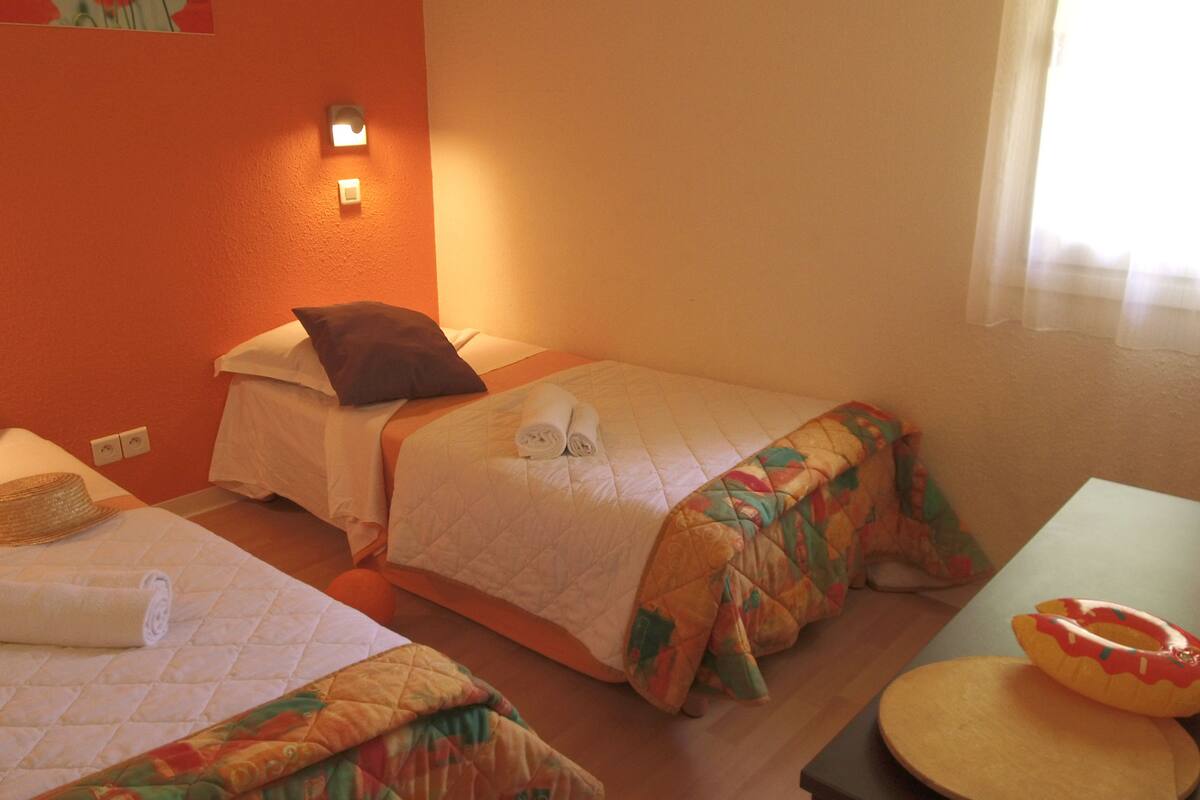 Een hotelkamer met twee bedden, elk voorzien van een opgerolde handdoek en een kussen. Er staat een klein tafeltje met een kaars en een decoratief object.