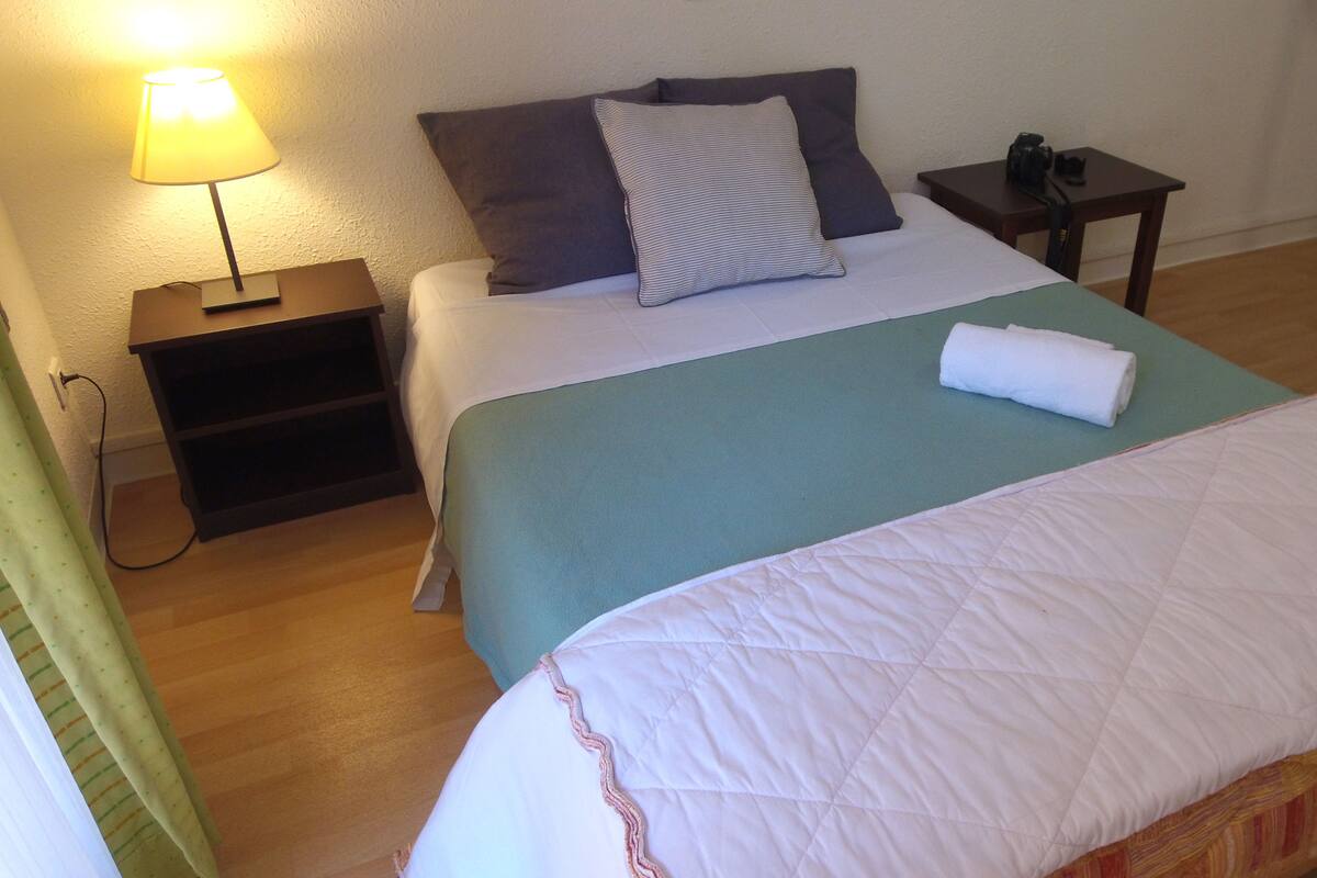 Een hotelkamer met een bed, nachtkastje, lamp en een klein tafeltje.