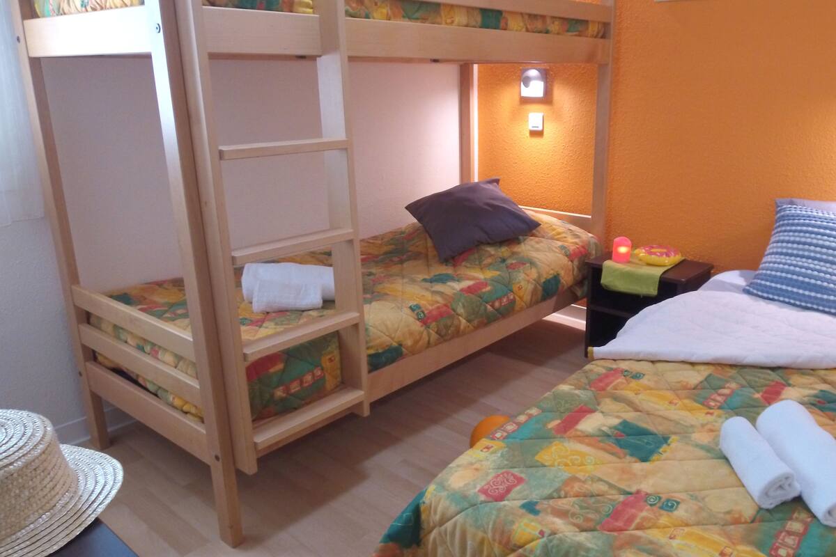 Een kamer met stapelbedden, een nachtkastje met een lamp en een bed met een opgerolde handdoek.