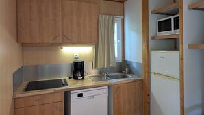 A compact kitchen with wooden cabinets, a sink, a dishwasher, a microwave, and a coffee maker. - VVF Sud Aveyron, Brusque (Brusque)