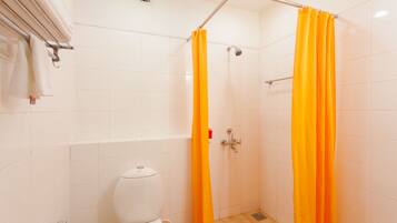 A bathroom with a white toilet, a shower with an orange curtain, and a towel rack with white towels.