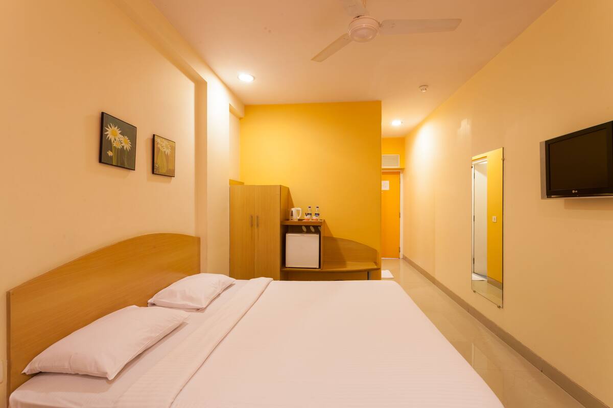 Una habitación de hotel con cama, escritorio, espejo, televisor y refrigerador pequeño.