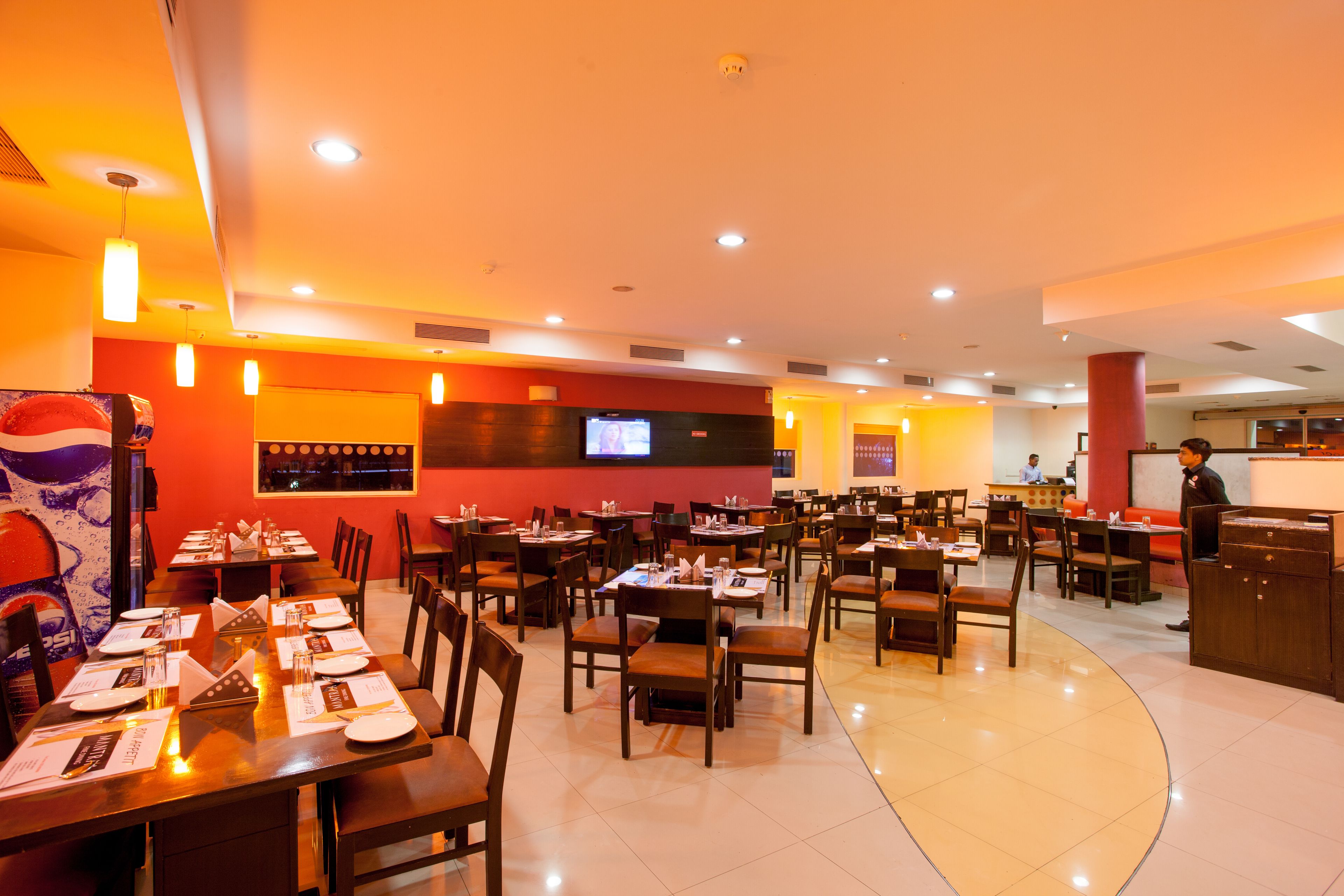 Un restaurante con varias mesas y sillas, una barra y una pantalla de televisión en la pared.