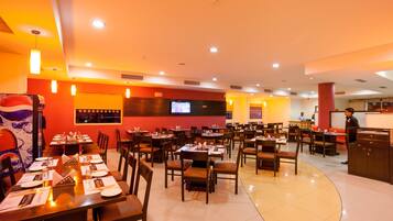 Un restaurante con varias mesas y sillas, una barra y una pantalla de televisión en la pared.