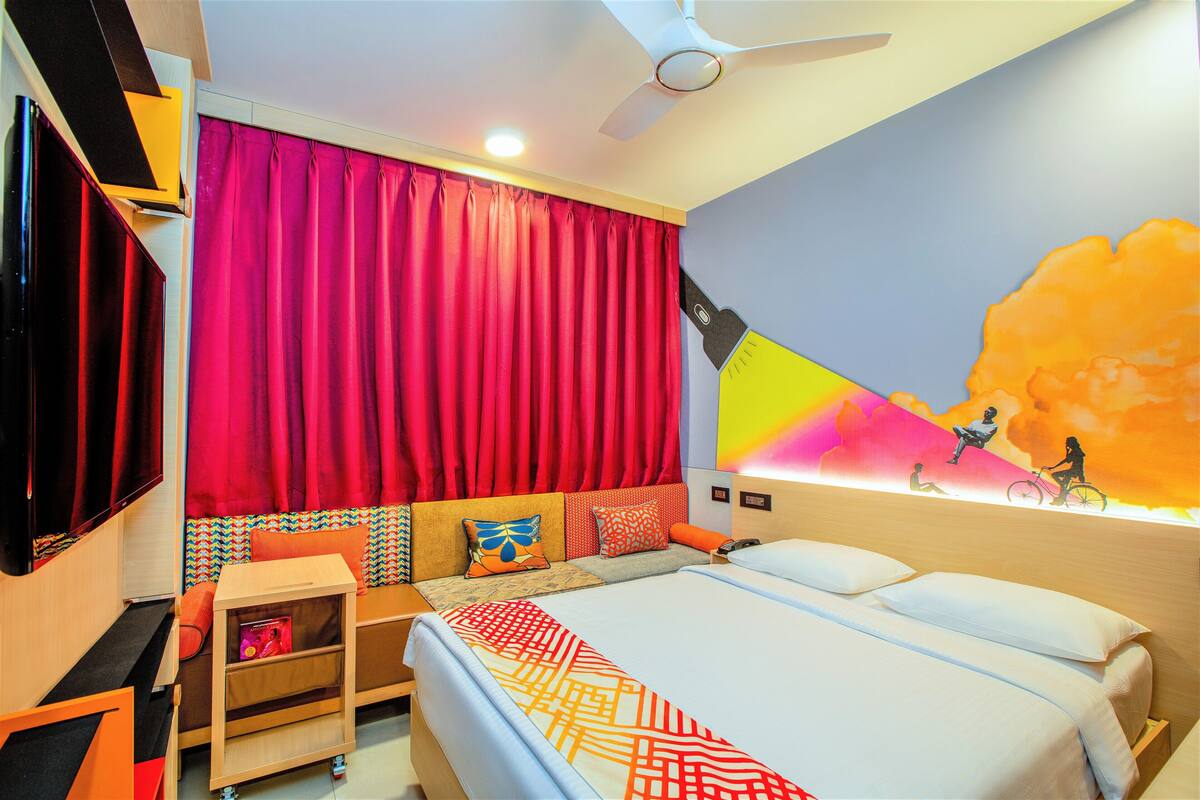Una habitación de hotel con cama, escritorio, silla, televisor y ventilador de techo.
