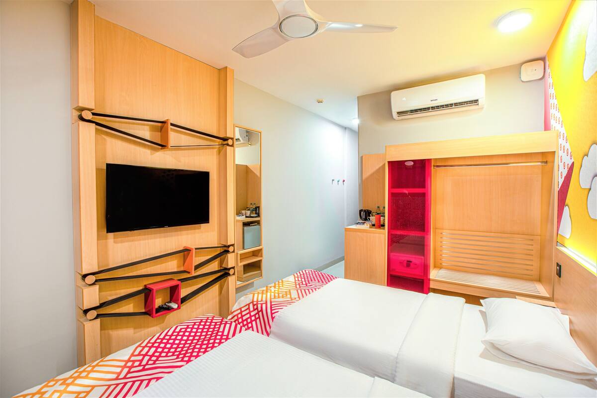 Habitación de hotel con cama, televisión montada en la pared, armario y ventilador de techo.
