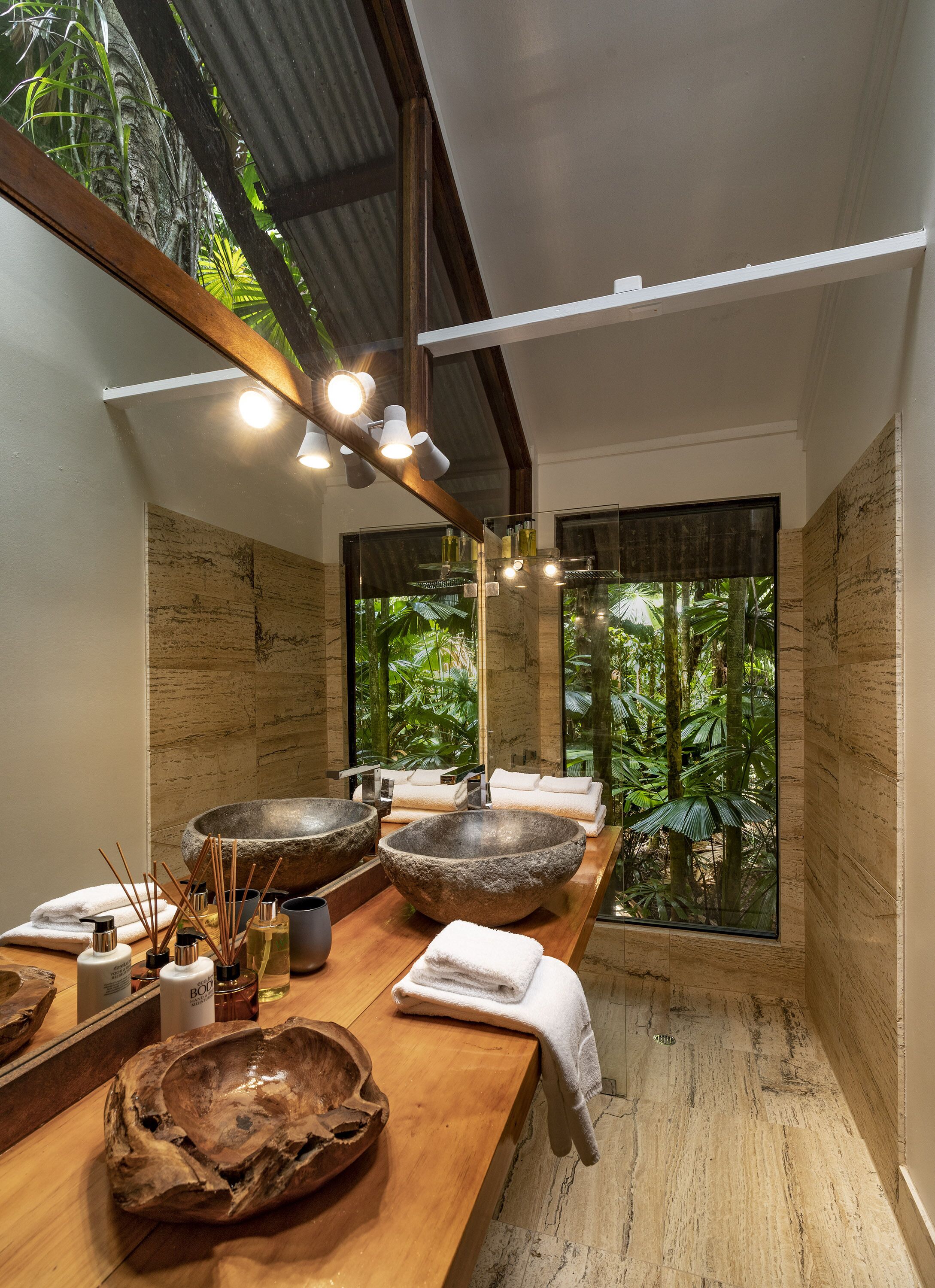 Une salle de bain moderne avec deux grands lavabos en pierre, un meuble-lavabo en bois et une grande fenêtre donnant sur un paysage verdoyant.