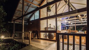 A wooden deck with a glass enclosure leading to a dining area with tables and chairs. - Daintree Wilderness Lodge (Diwan)