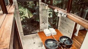 A modern bathroom with a wooden vanity, a large mirror, and a view of lush greenery outside. - Daintree Wilderness Lodge (Diwan)
