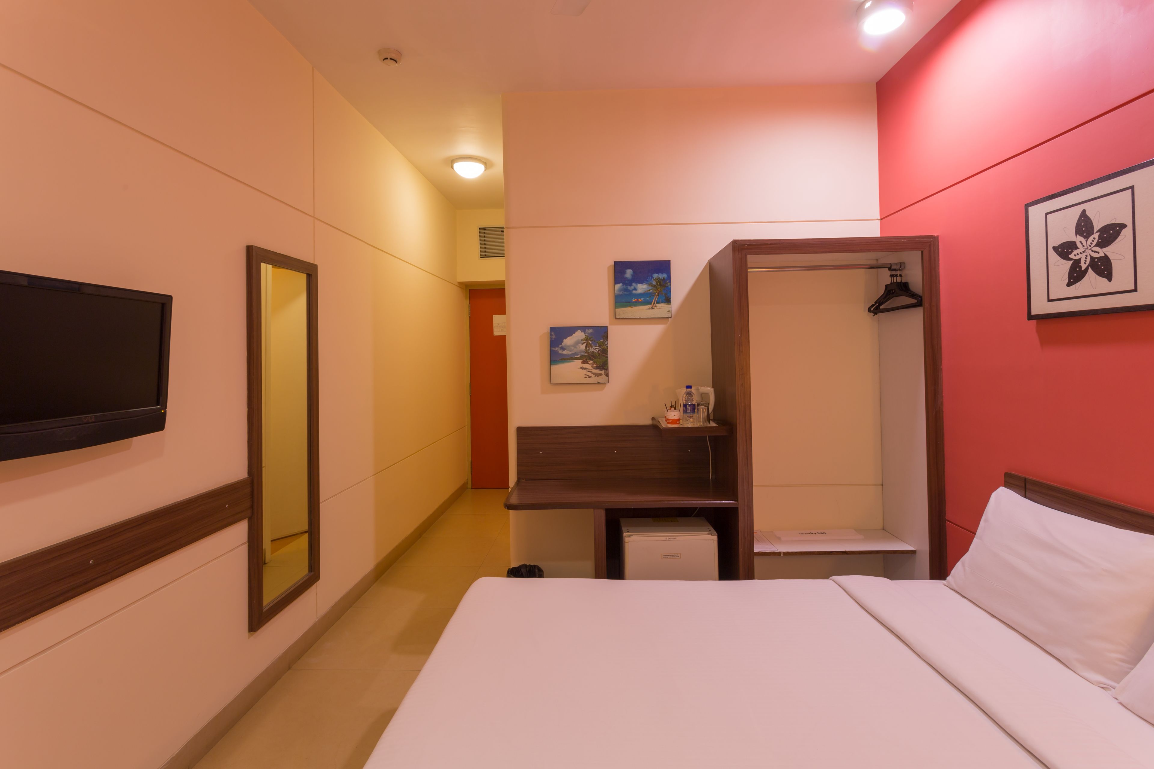 A hotel room with a bed, a TV, a mirror, a small desk, and a shower area.