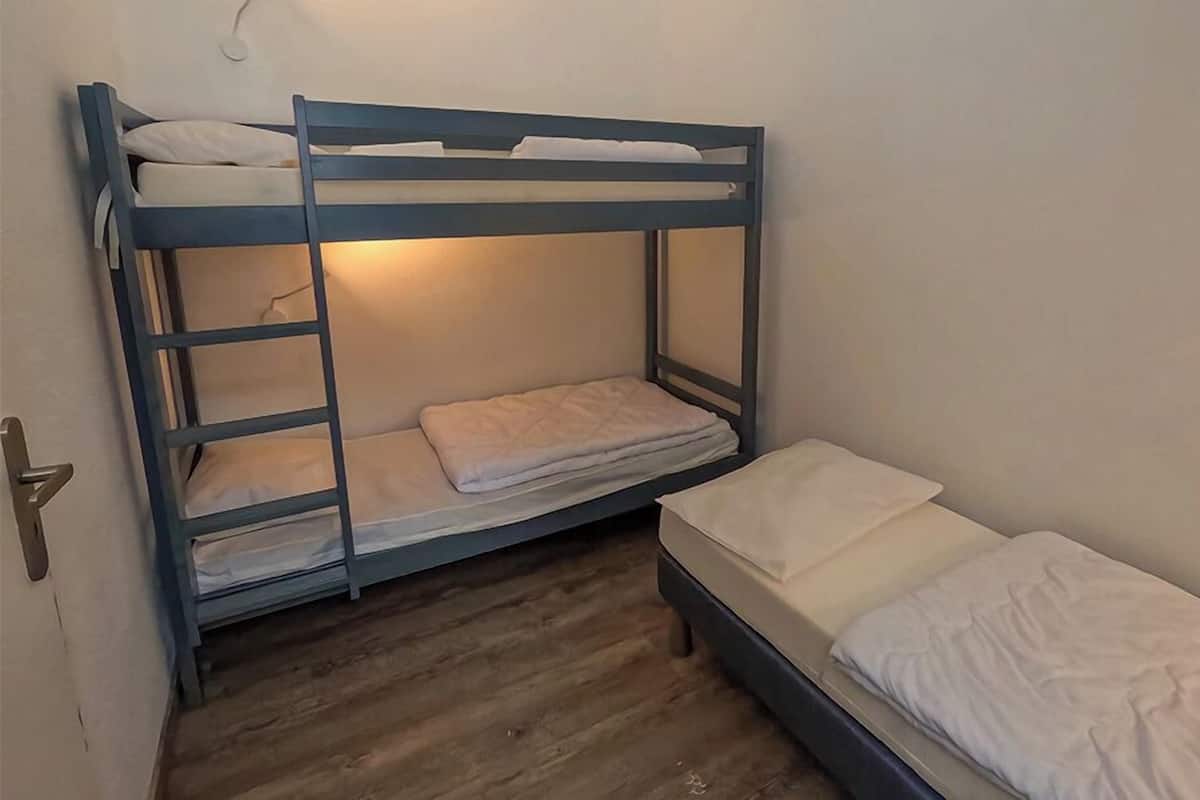 A bunk bed room with a wooden floor and white bedding.