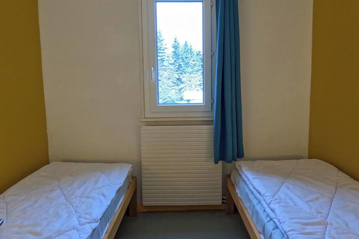 A small room with two single beds, a window with a view of trees, and a radiator.
