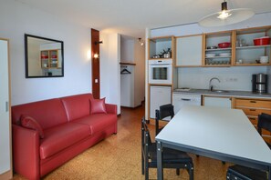 Eine kleine Küche mit Esstisch, rotem Sofa und einem Spiegel an der Wand.