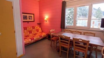 Une pièce avec une table et des chaises en bois, un mur rouge, une fenêtre donnant sur des arbres et une porte.