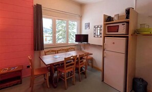 A compact kitchen with a dining table, chairs, a refrigerator, a microwave, and a television. -  Résidence Vacancéole Les Monts Jura   (Lelex)