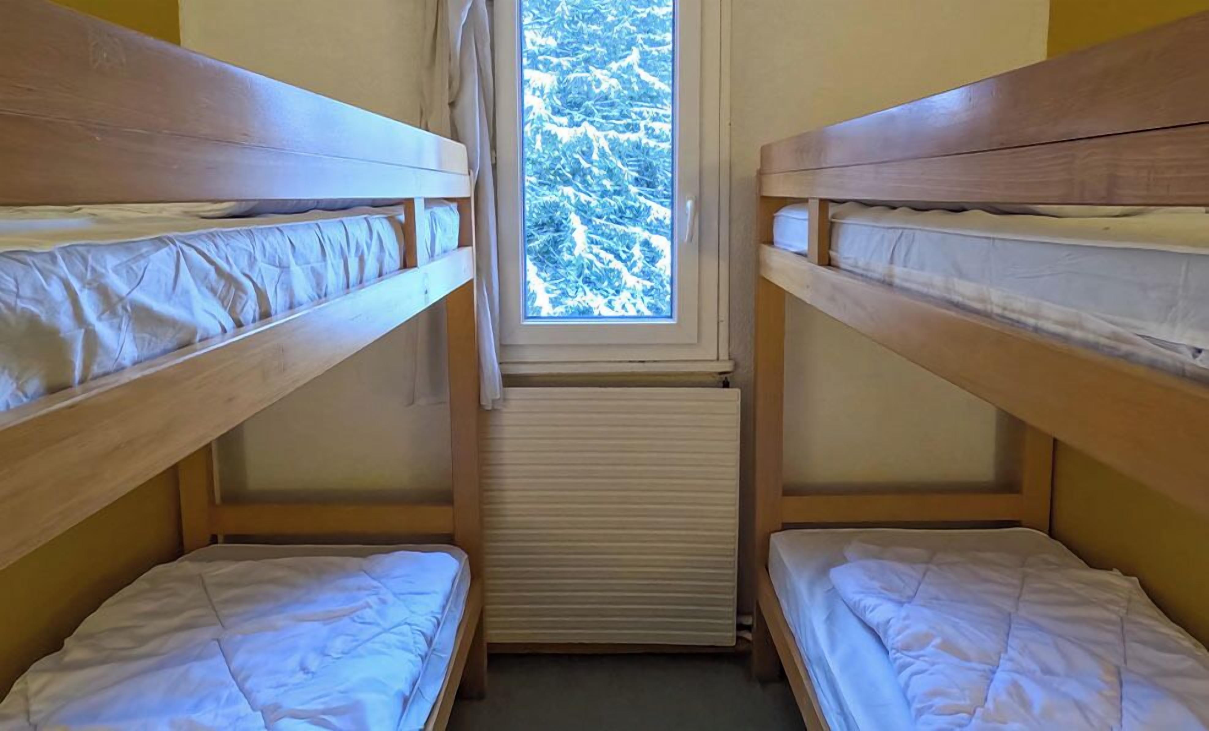 Un dormitorio con dos literas y una ventana que ofrece vistas a árboles cubiertos de nieve.