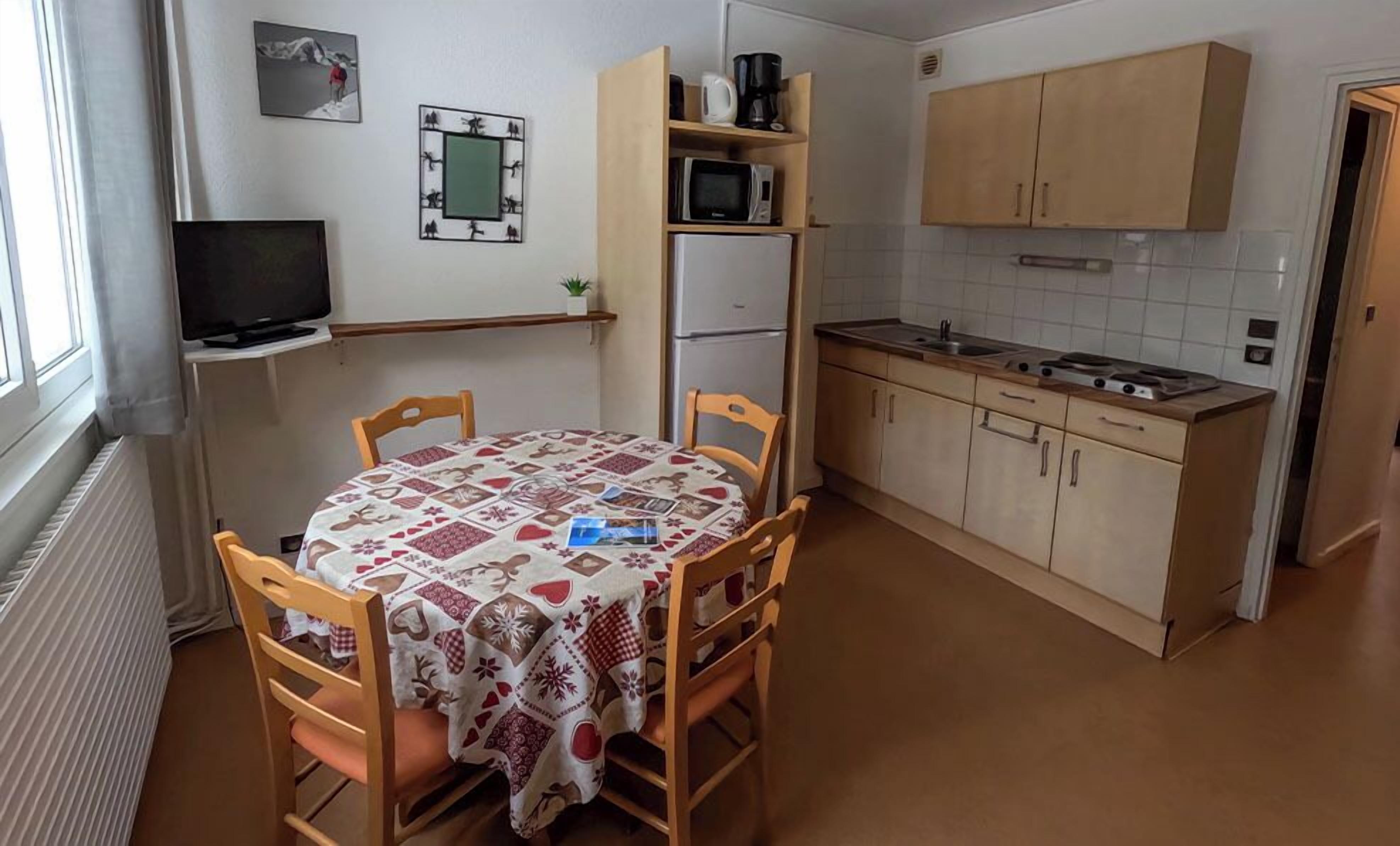 A compact kitchen with a dining table, chairs, a microwave, a refrigerator, and wooden cabinets.