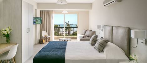 A modern hotel room with a large bed, a desk, a chair, and a balcony with a view of the sea.