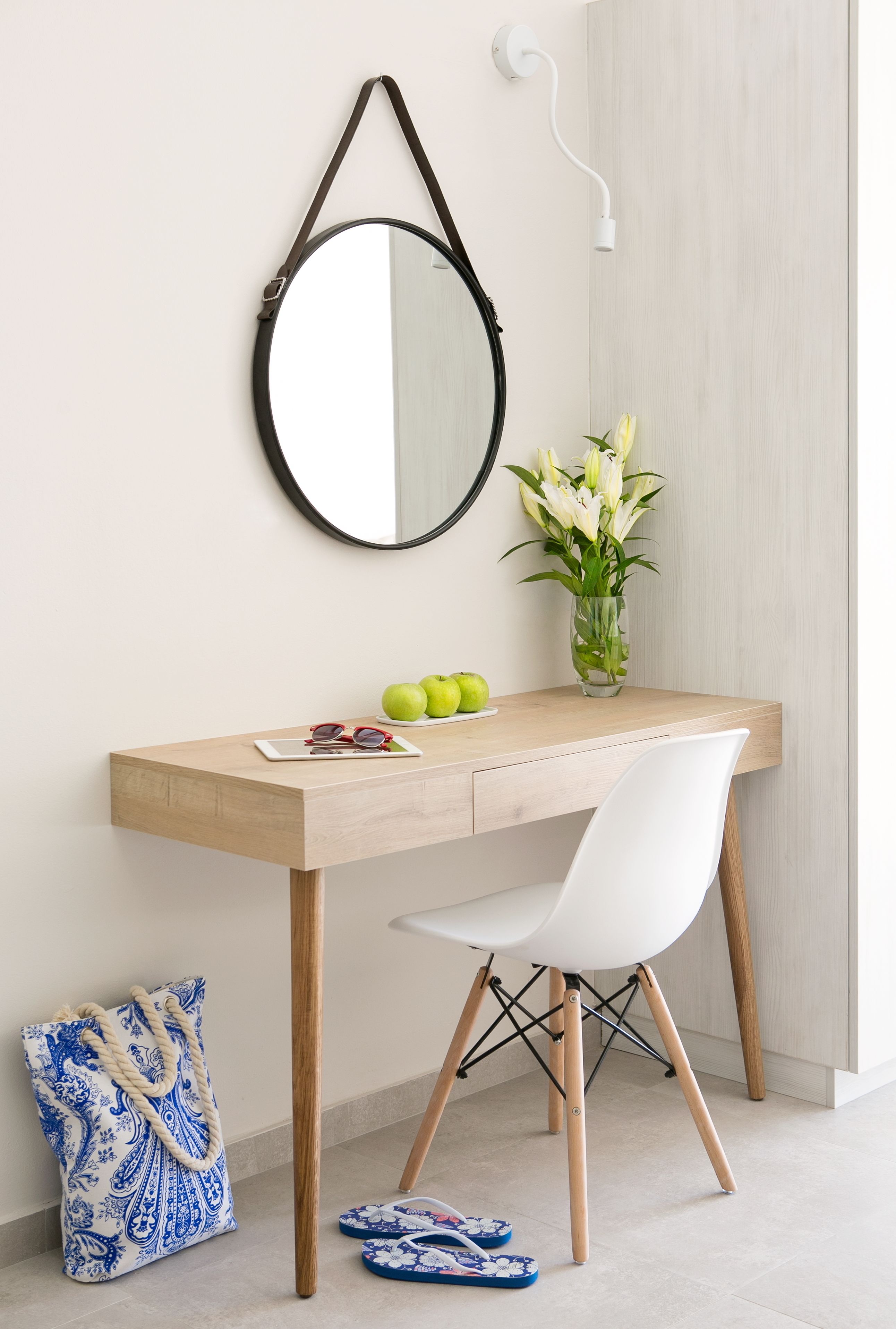 A modern desk with a mirror, a vase of flowers, and a pair of glasses on the surface.