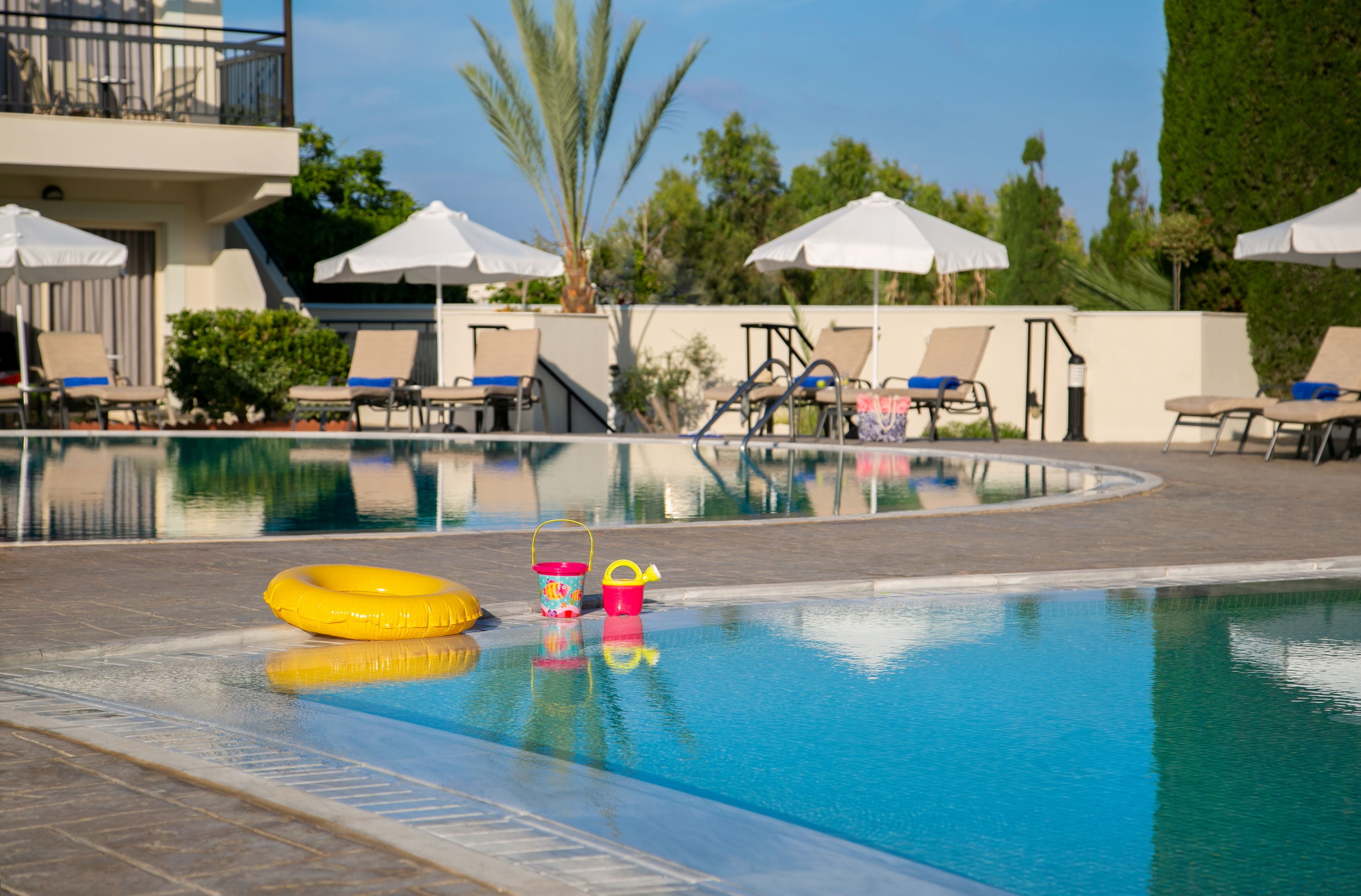 Ein Swimmingpool mit Liegestühlen und Sonnenschirmen, umgeben von viel Grün.
