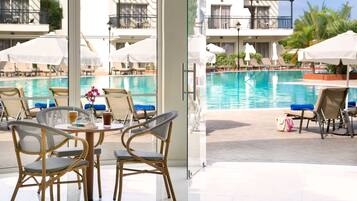 A poolside area with wicker chairs, umbrellas, and a view of a swimming pool.