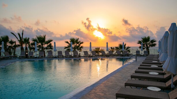 Zona junto a la piscina con sillones de descanso y sombrillas, con vistas al mar al atardecer.