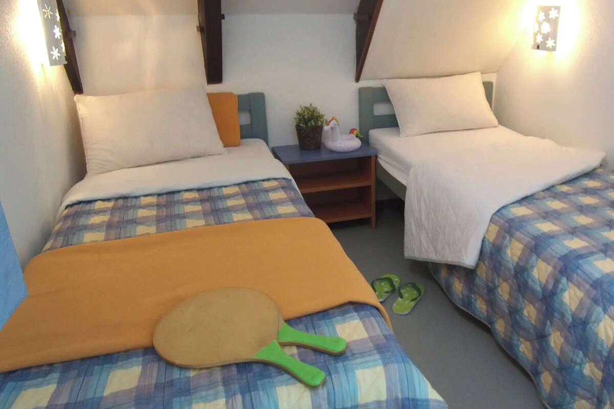 Une chambre d’hôtel avec deux lits, chacun recouvert d’une courtepointe à carreaux, une table de chevet avec une lampe et une petite plante.