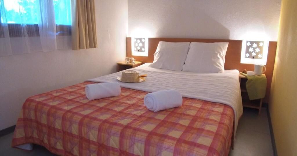 Een hotelkamer met een bed, twee nachtkastjes, een raam met gordijnen en een wandlamp.