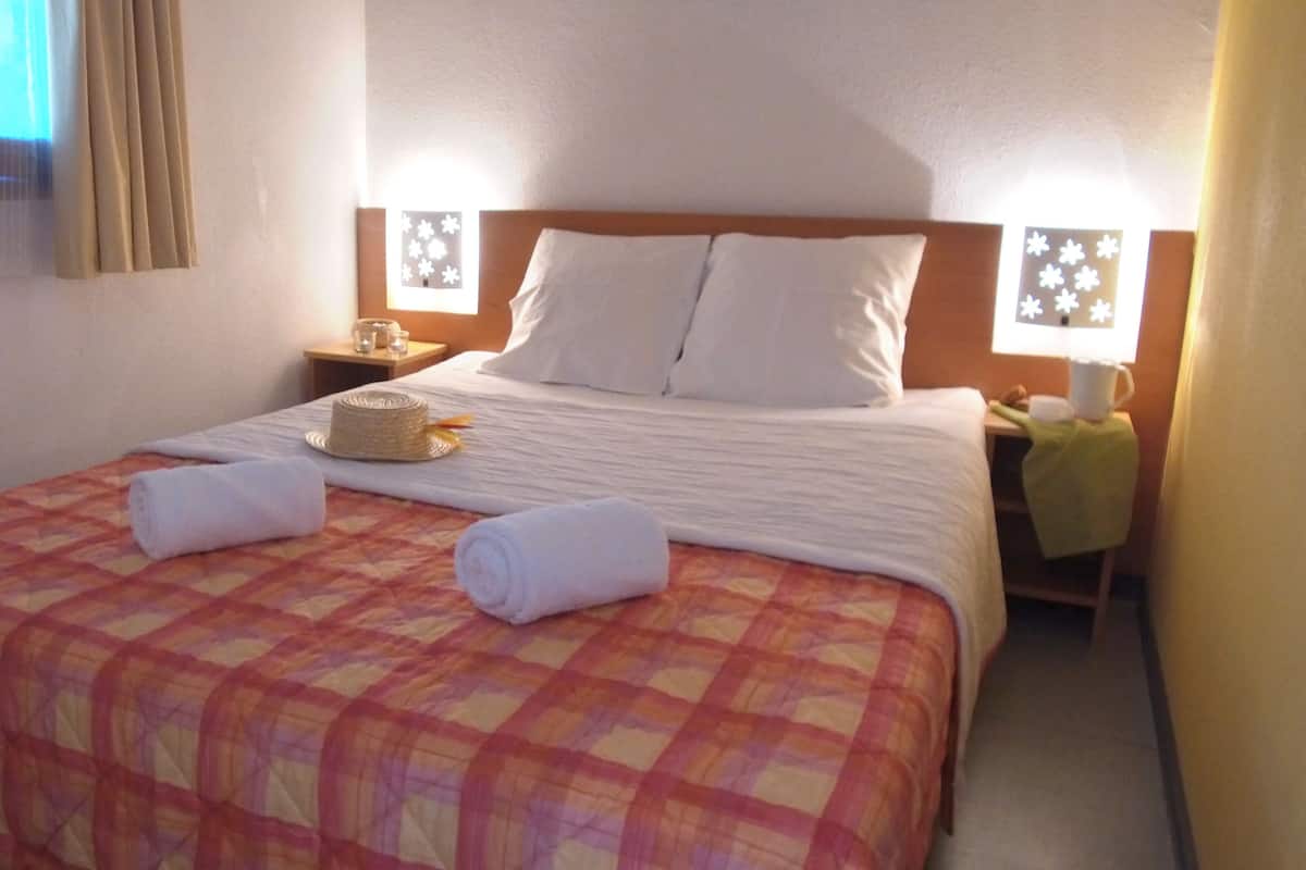 Quarto de hotel com uma cama grande, duas mesas de cabeceira e uma janela com cortinas.