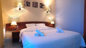 A neatly made bed with white linens and two rolled towels, two bedside lamps, and three framed pictures on the wall.