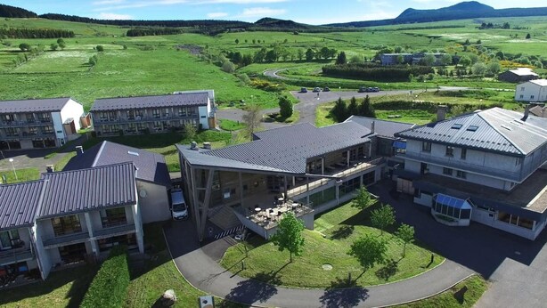 A modern building with a courtyard, surrounded by green fields and a winding road.