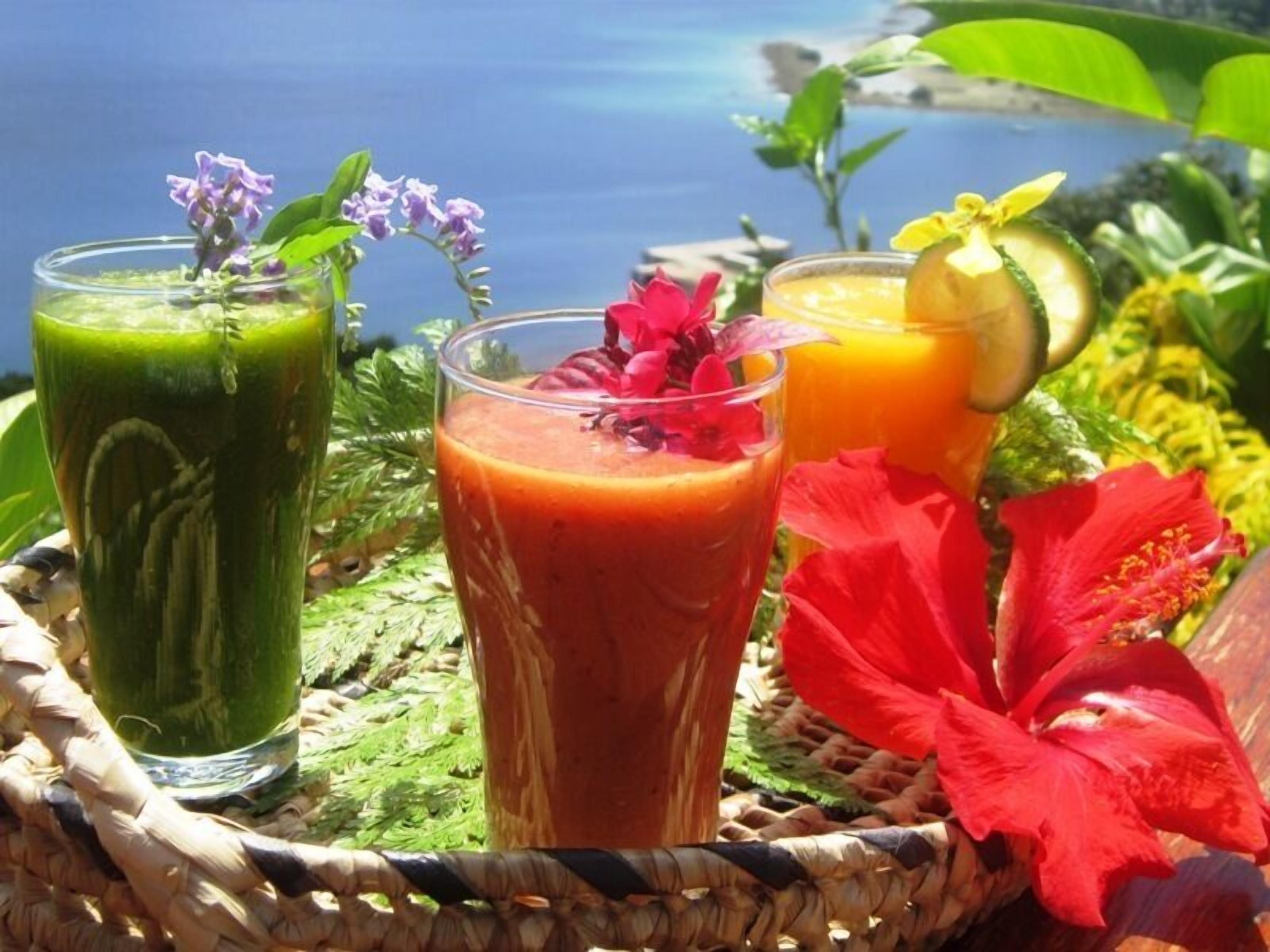 Trois verres de jus de fruits sur un plateau en osier, avec un décor tropical en arrière-plan.
