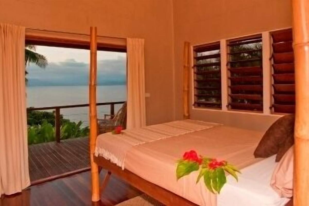 A bedroom with a bed, a window with shutters, and a view of the sea.