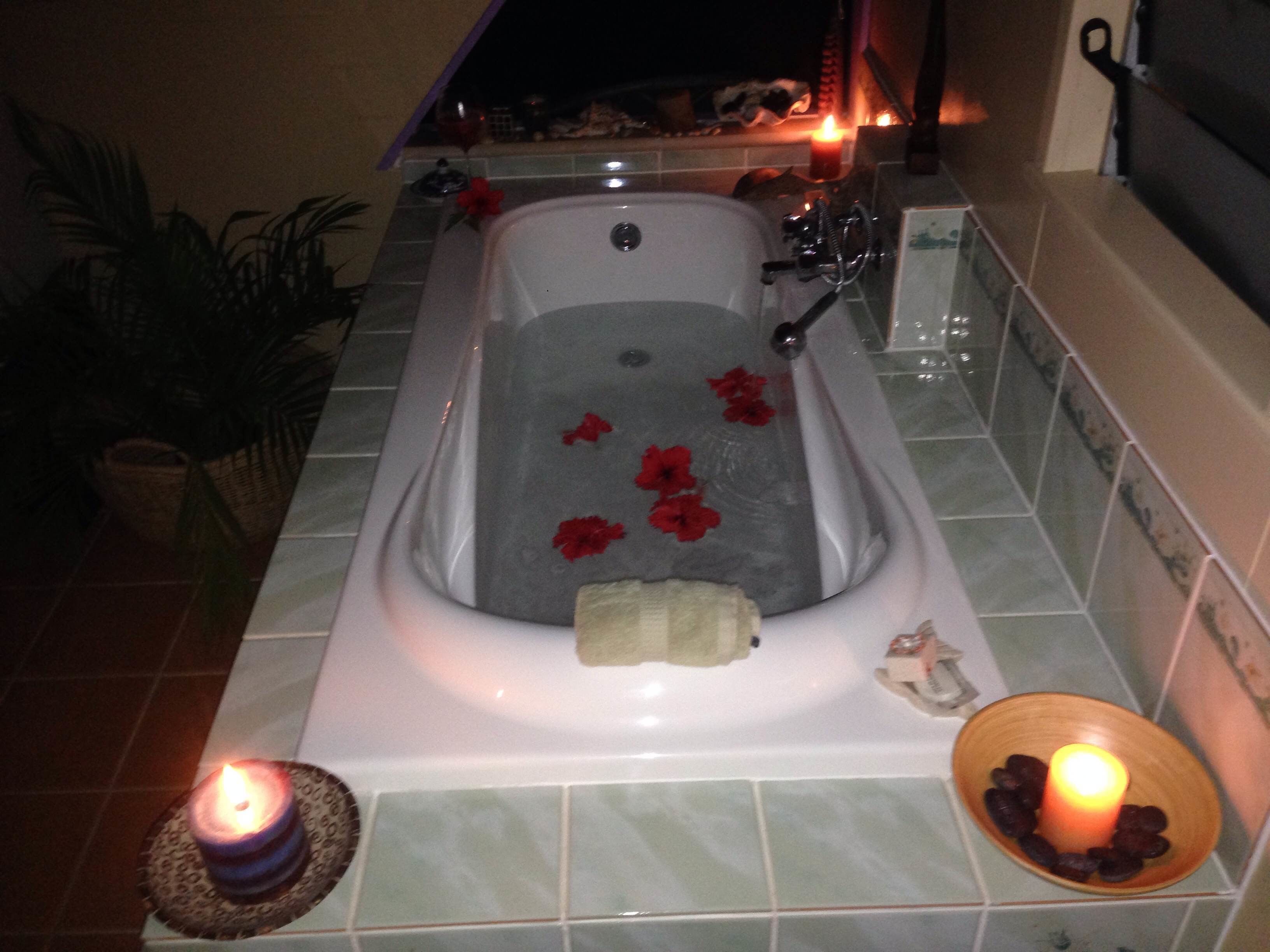 Una bañera con flores rojas, velas y una alfombra de baño.