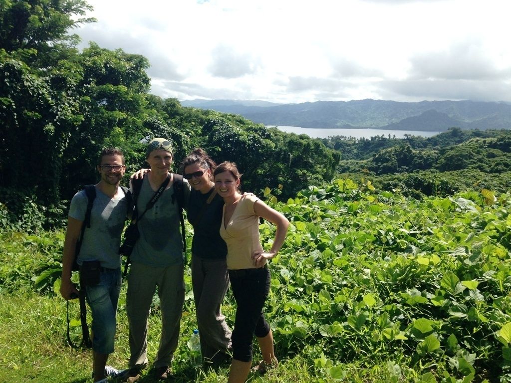 A group of people standing on a grassy hill with a lake and mountains in the background.