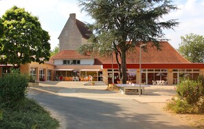 Stunning building with a red-tiled roof and conical tower, offering outdoor seating areas and a lush, landscaped setting.