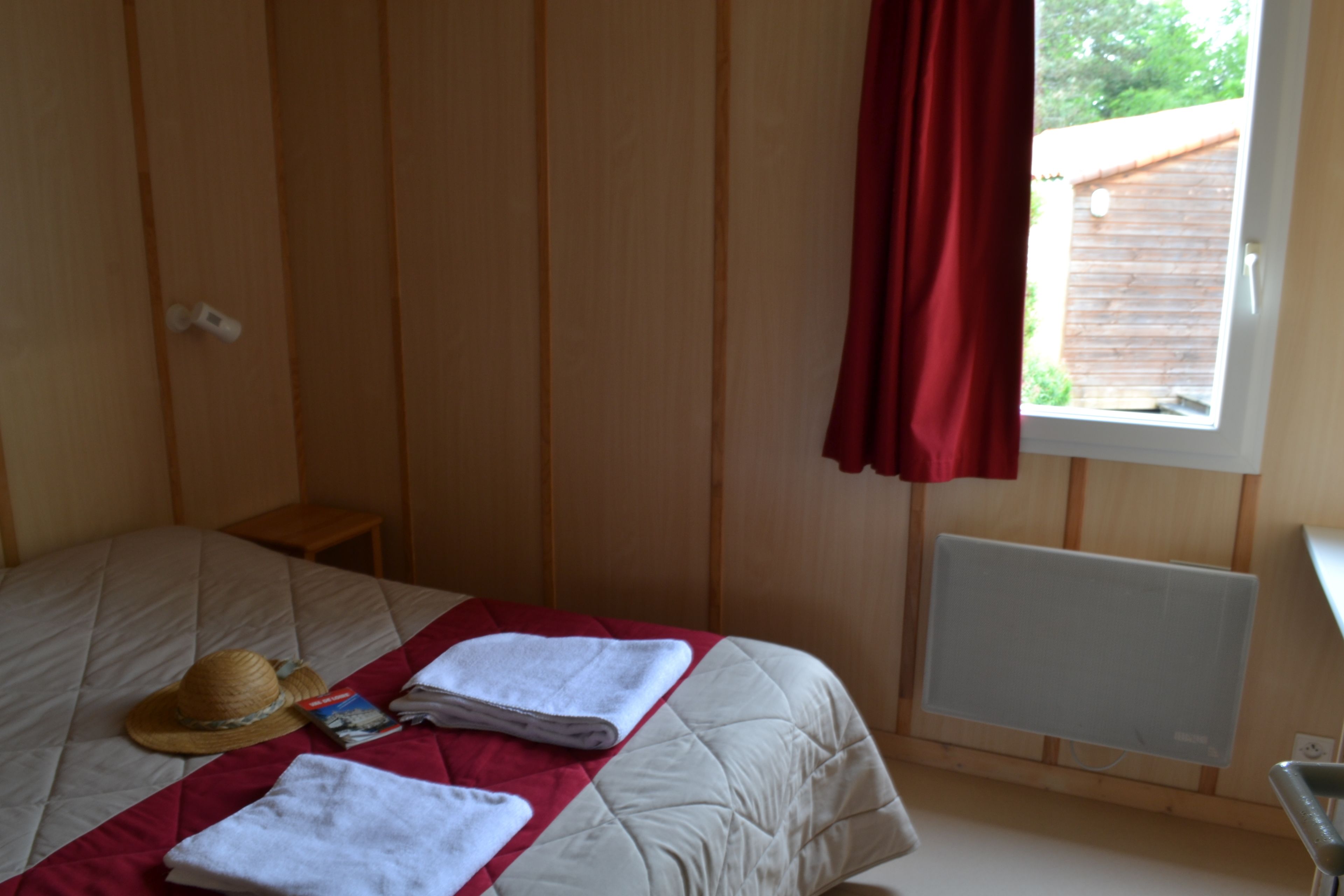 Une chambre à coucher avec un lit, une fenêtre ornée d’un rideau rouge, un radiateur et une petite table de chevet.
